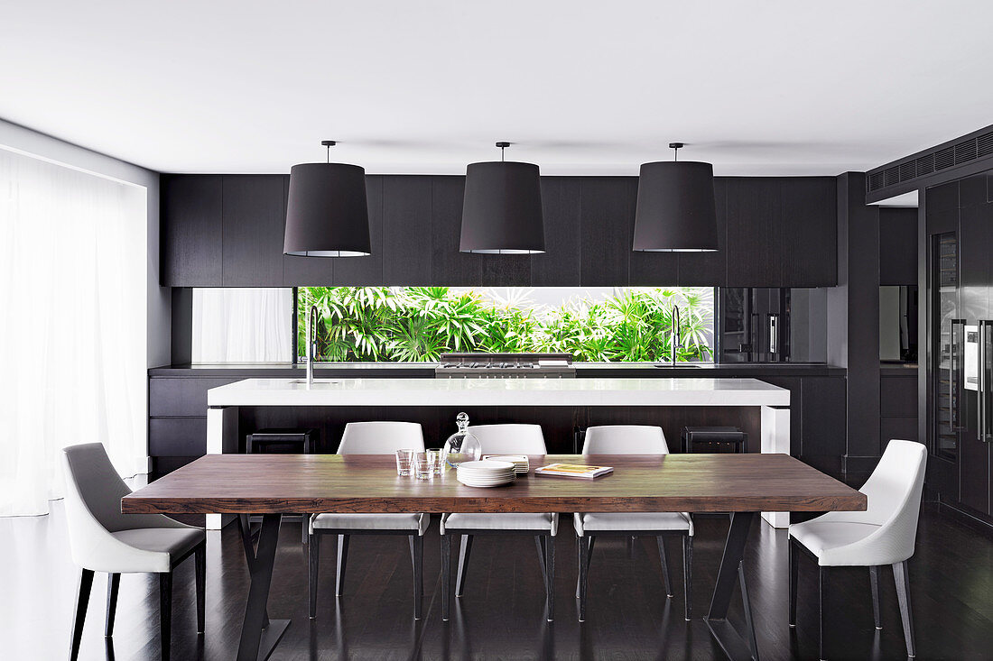 Langer Esstisch mit Holzplatte und Designer-Stühle vor weisser Kücheninsel in offenem Wohnraum