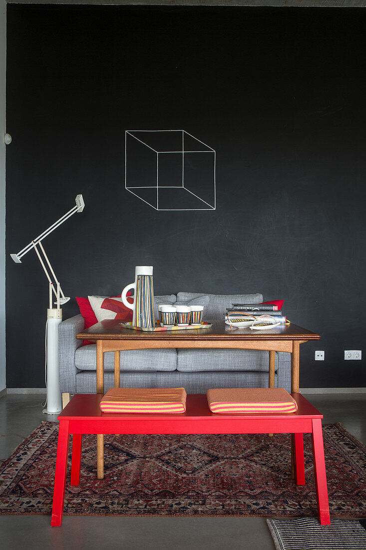 Red bench, wooden table and sofa against wall painted with chalkboard paint