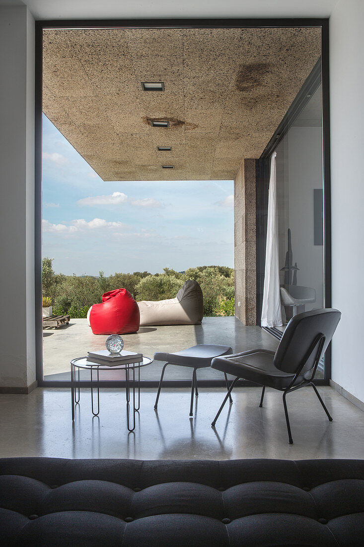 Eleganter Stuhl mit Fussschemel und Beistelltisch vor Glaselement, Blick auf die Terrasse