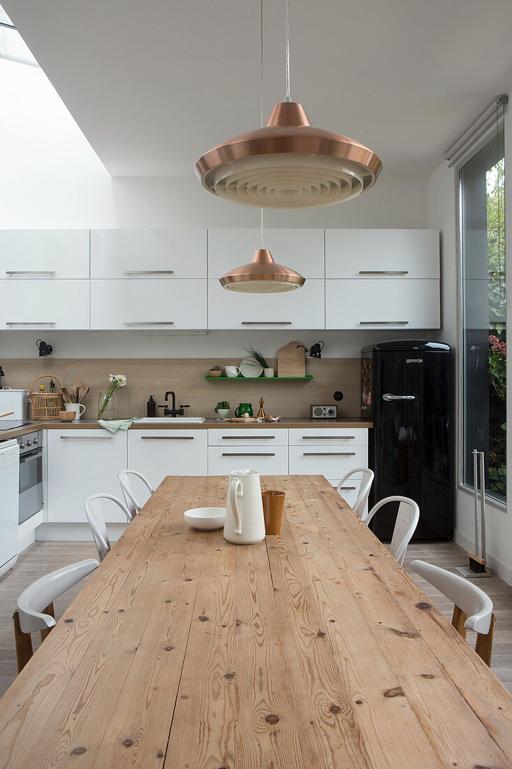 Long wooden table and chairs in white, open-plan kitchen