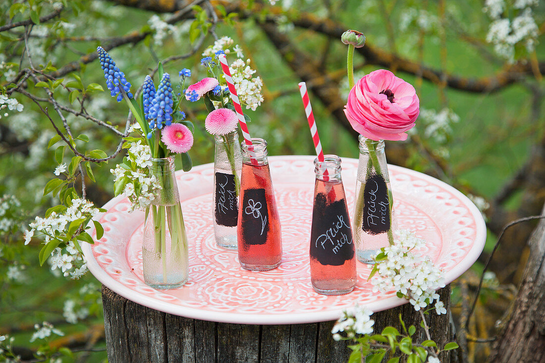 Beschriftete Limonadenflaschen und Blumen auf Tablett im Garten