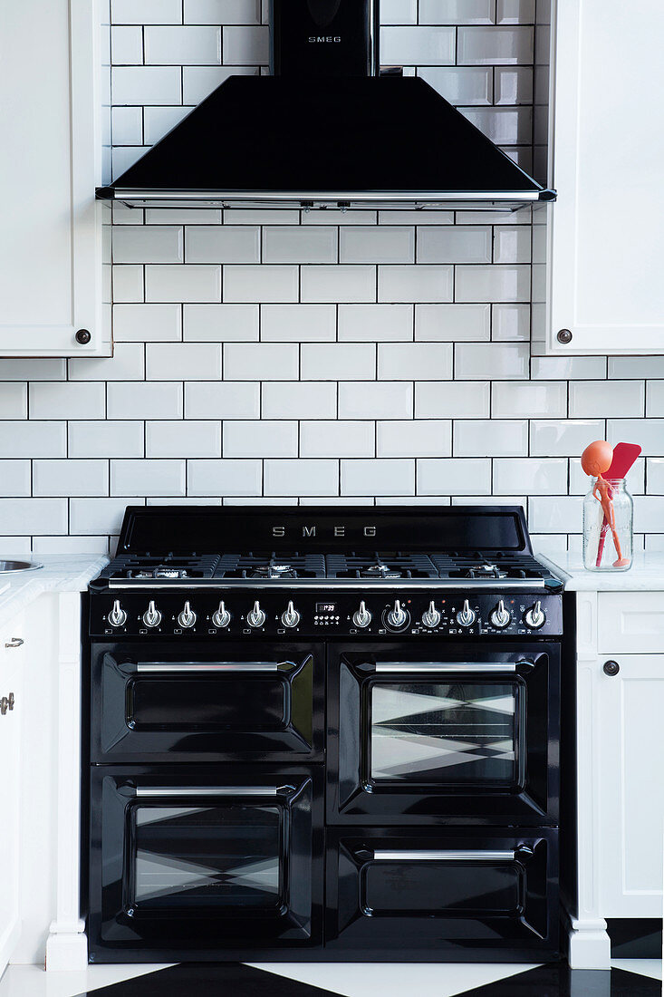 Schwarzer Gasherd und Abzugshaube vor Wand mit weißen U-Bahn-Fliesen in der Küche