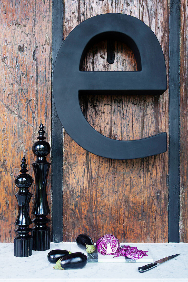 Black decorative letter on rustic wooden wall above vegetables and kitchen utensils on worksurface