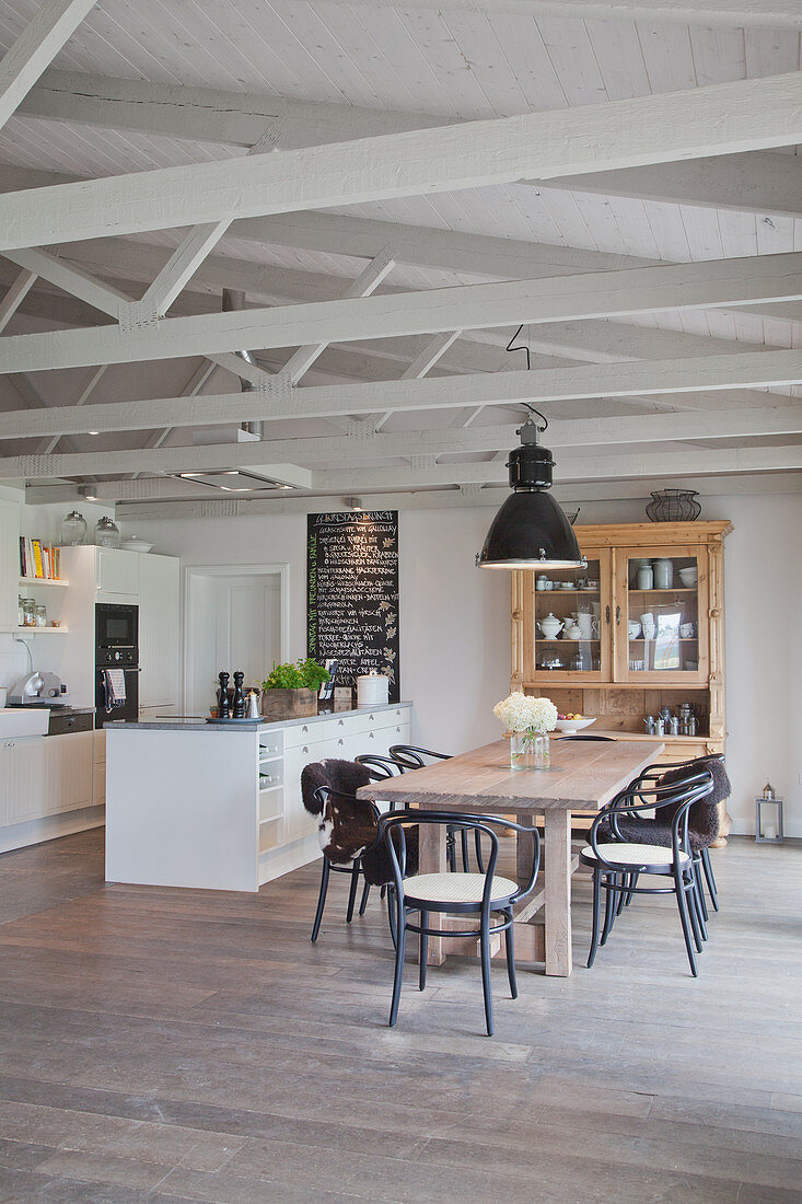 weiße Küche mit Kücheninsel und Holztisch mit Stühlen in offenem Wohnraum in umgebautem Stall