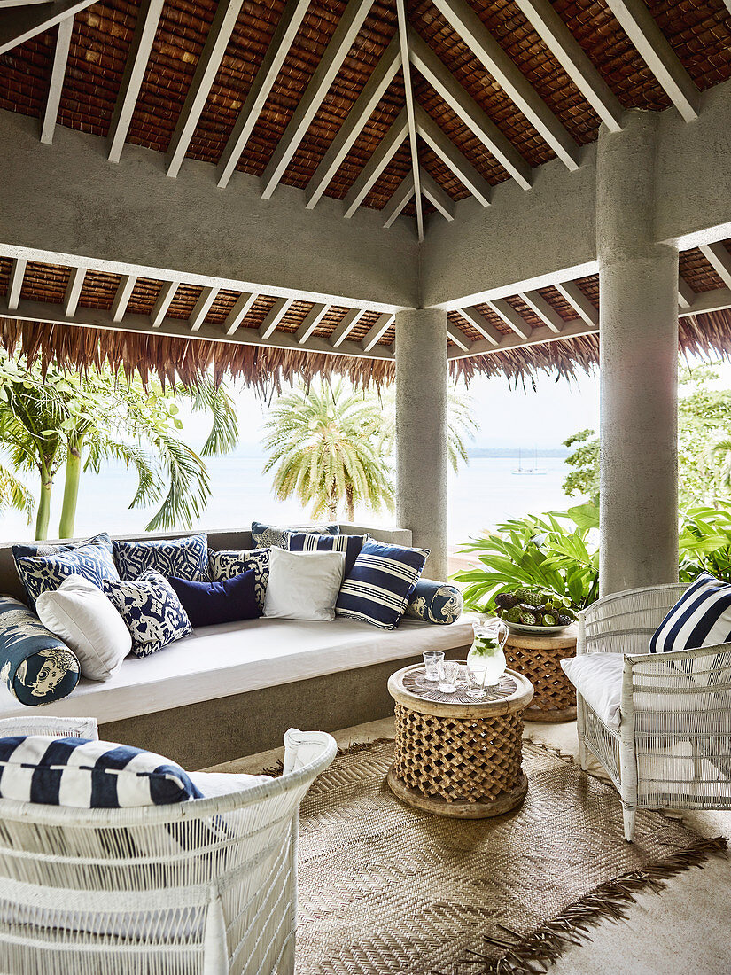 Outdoormöbel mit blau-weiß gemusterten Kisssen auf überdachter Terrasse mit Meerblick