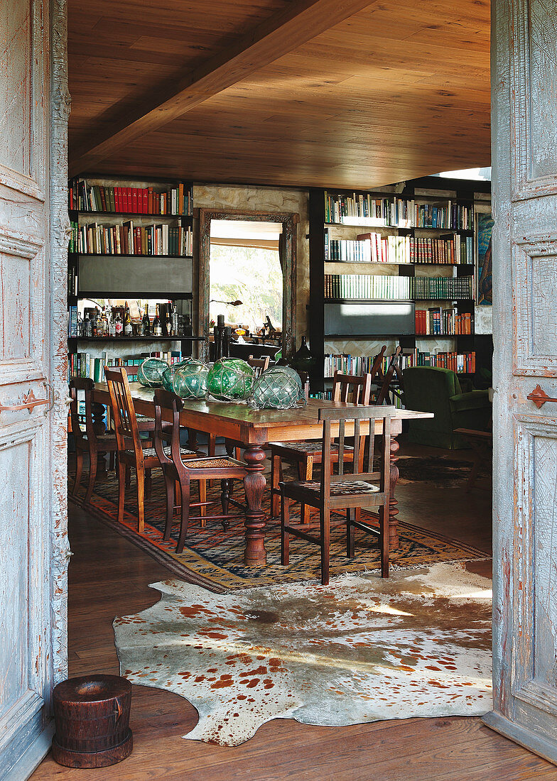 View through open wooden doors into dining room with long table, chairs and bookcases