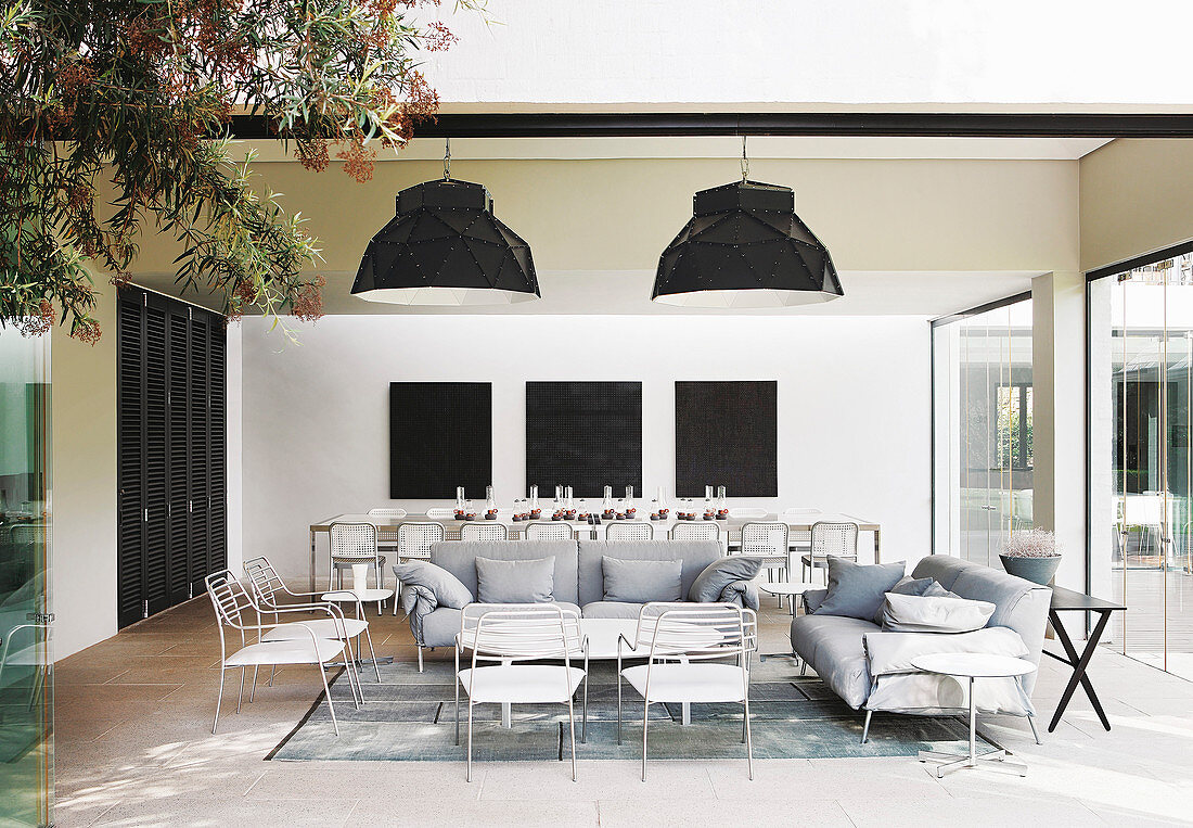 Loungebereich mit weißen und hellgrauen Möbeln, im Hintergrund langer Esstisch