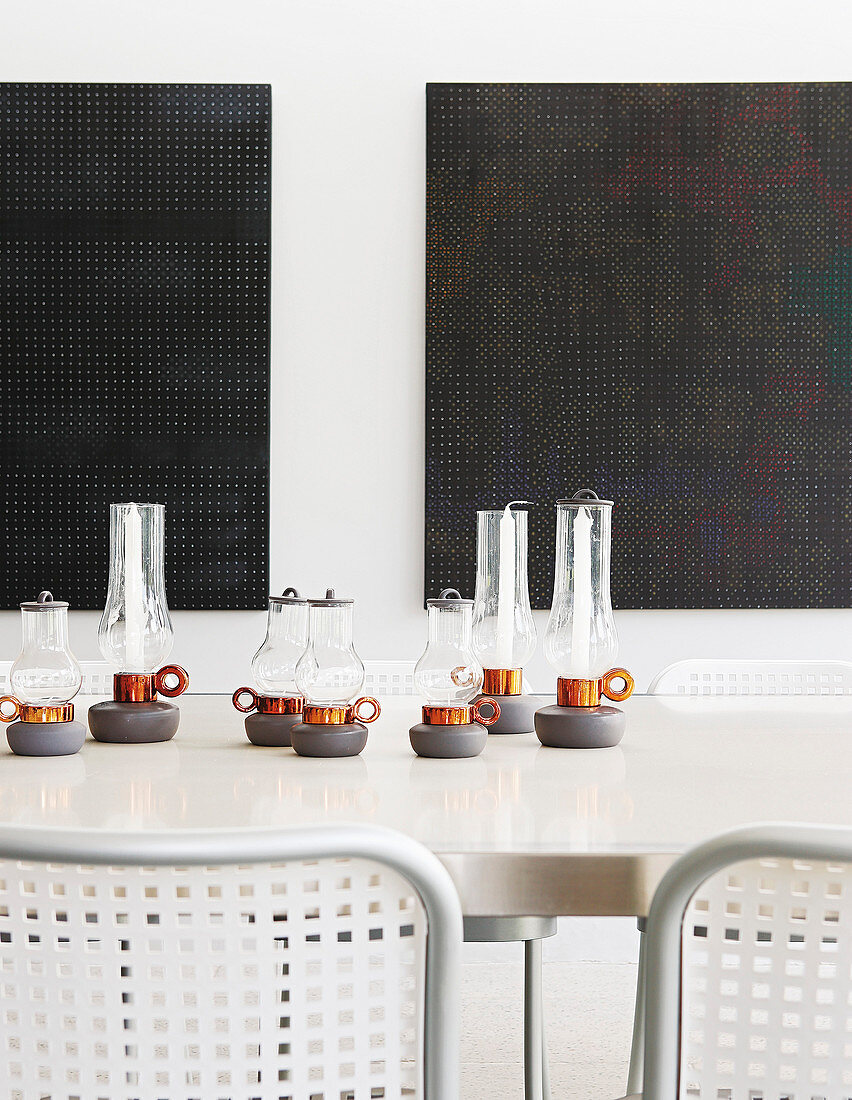Candle lanterns on long dining table in front of black artworks on wall
