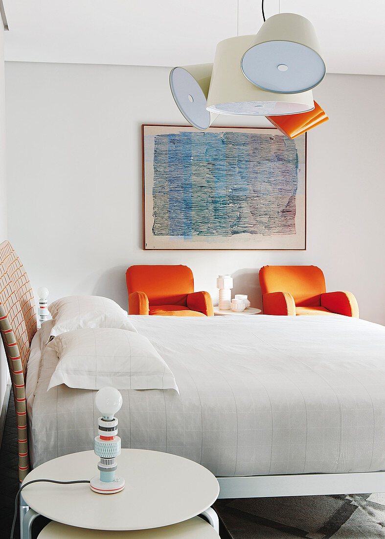Doppelbett und Beistelltisch mit zwei orangefarbenen Sesseln in hellem Schlafzimmer