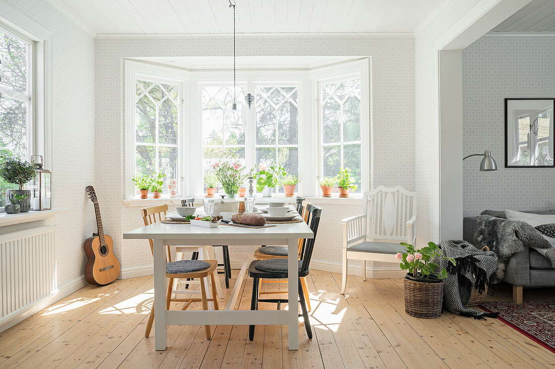 White dining table with various chairs in front of bay window