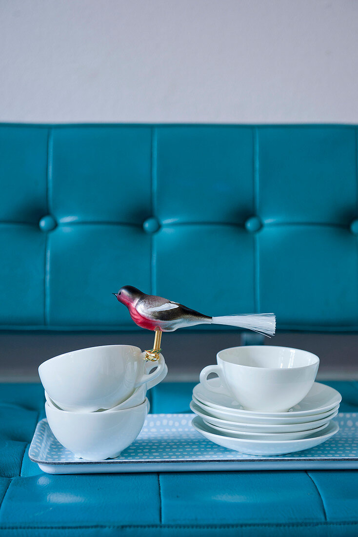 Tray of crockery and bird ornament on blue sofa