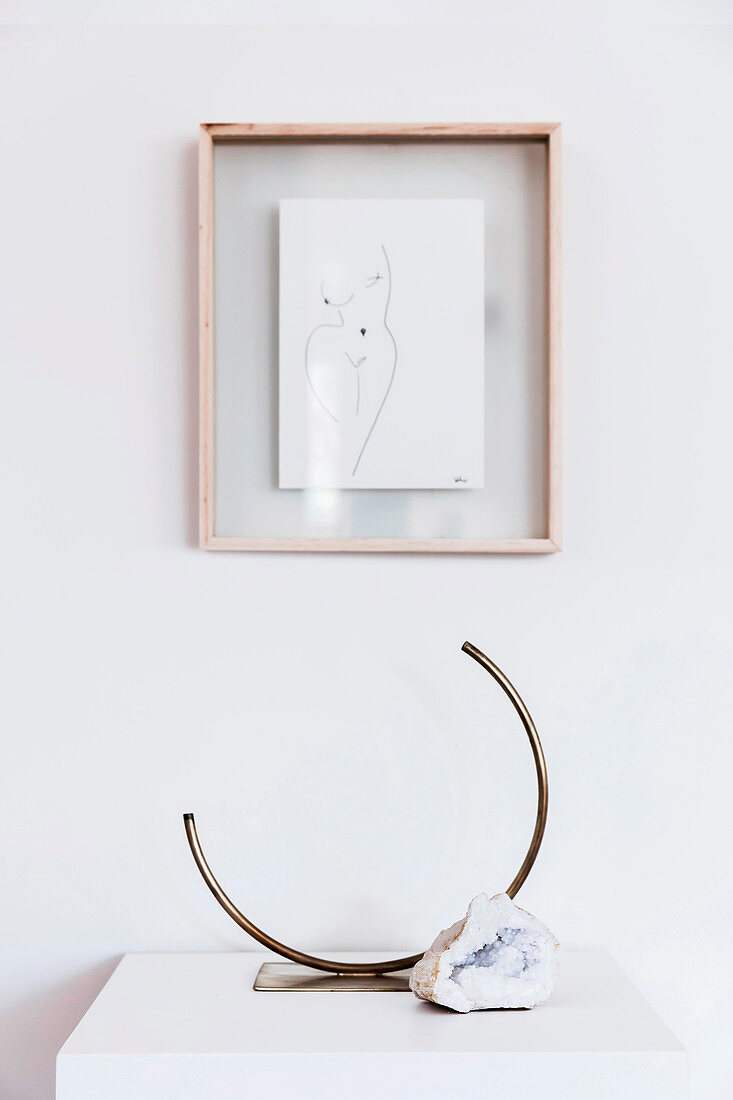 Framed drawing on white wall, including designer brass vase and natural stone
