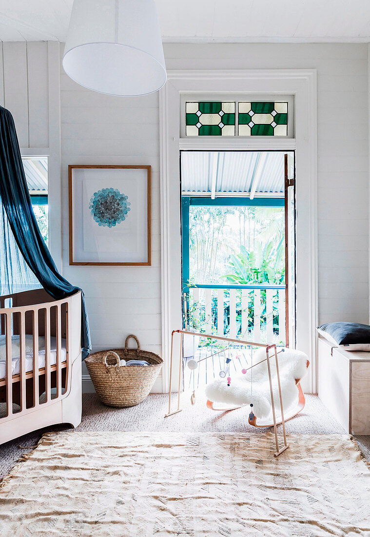 Mobile und Babywiege vor Balkontür und Gitterbett mit Baldachin im Babyzimmer