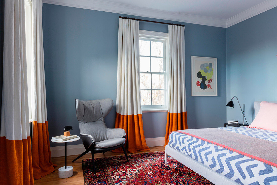 Grauer Ohrensessel, Beistelltisch und Doppelbett in graublauem Schlafzimmer