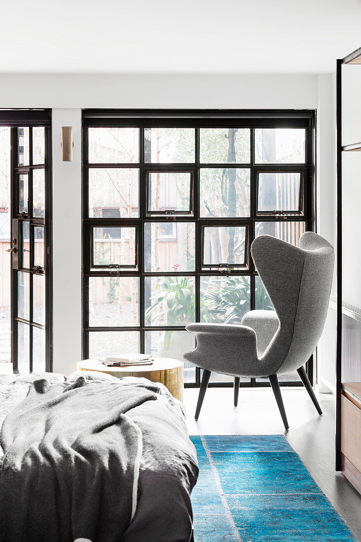 Doppelbett, Beistelltisch und Ohrensessel im Schlafzimmer mit Industriefenster