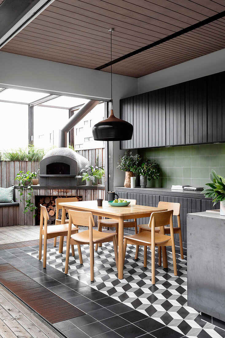 Schwarze Küchenzeile mit grünen Wandfliesen und Essbereich, im Hintergrund Pizzaofen auf der Terrasse
