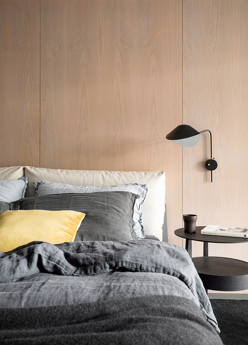 Doppelbett und Wandlampe an Raumteiler mit Holzverkleidung