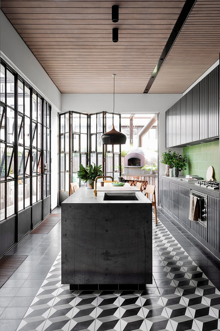 Black kitchen unit with green wall tiles and kitchen island, pizza oven on the terrace in the background