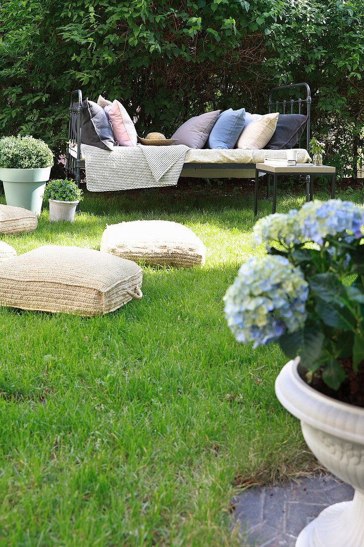 Floor cushions on lawn and metal bed used as couch in summery garden