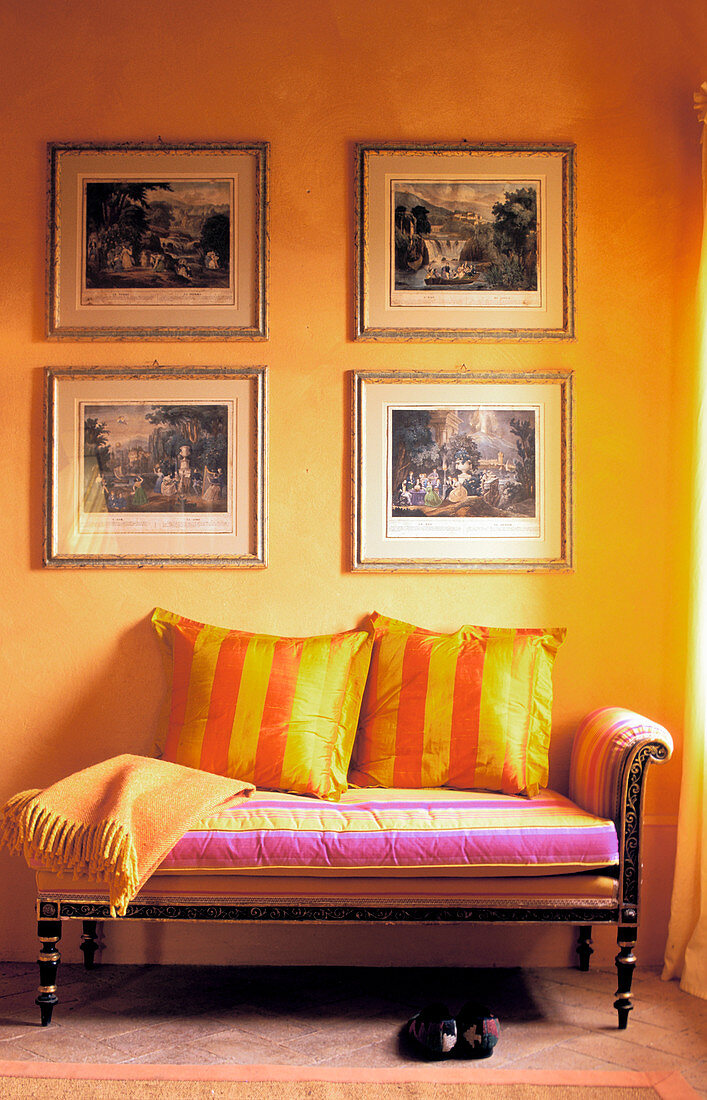 Four pictures on yellow wall above antique couch with striped scatter cushions
