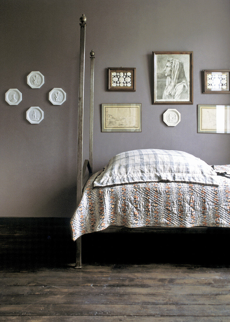 Metal bed below old pictures and decorative plates on grey wall