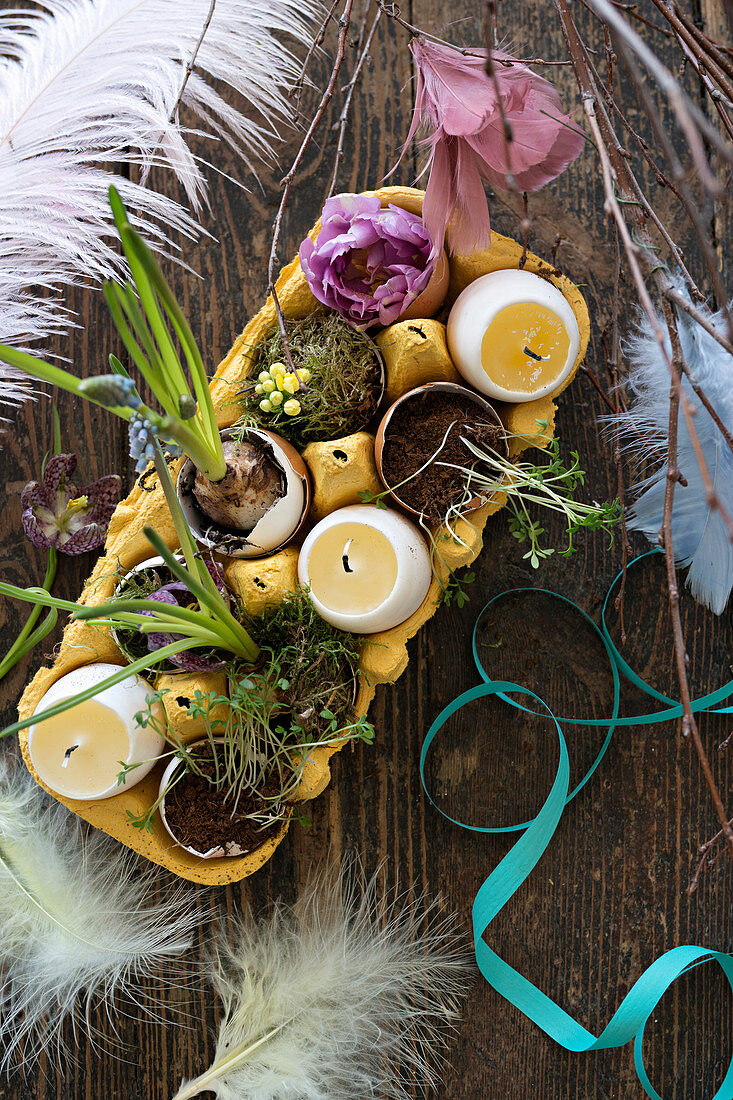 Osterdeko mit Eierkerzen und Blumen in Eierschalen im gelben Eierkarton