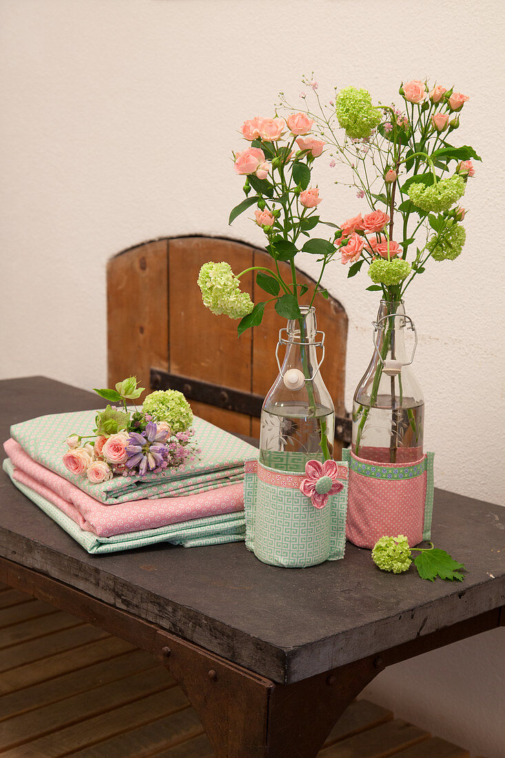 Flowers in swing-top bottles with fabric covers next to stacked folded fabrics