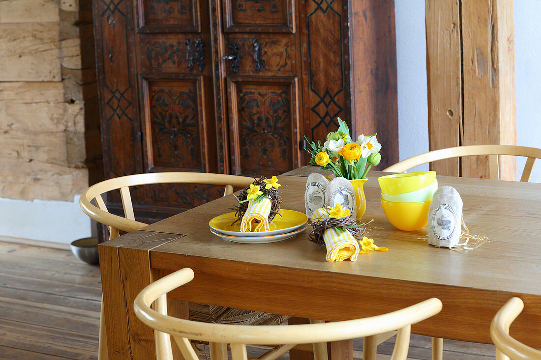 Gelbes Geschirr, Servietten mit Osterkränzchen, Stoffsäckchen mit Hasenmotiv und kleiner Blumenstrauß auf Tisch