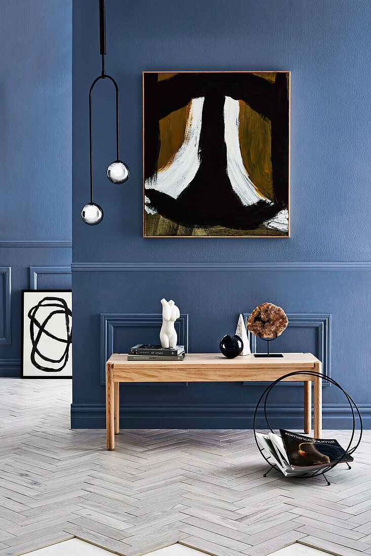 Console table with decorative objects, magazine holder, pendant lamp and artwork on a blue wall