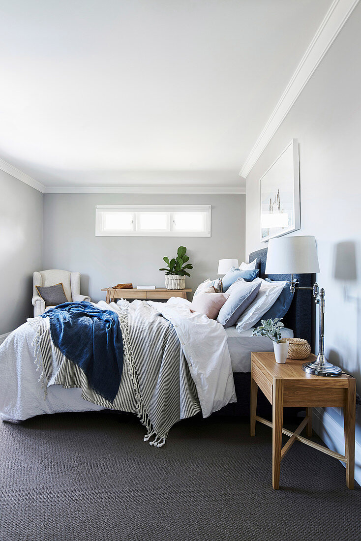 Doppelbett mit Kissen und blauem Bettkopfteil im Schlafzimmer mit hellgrauen Wänden