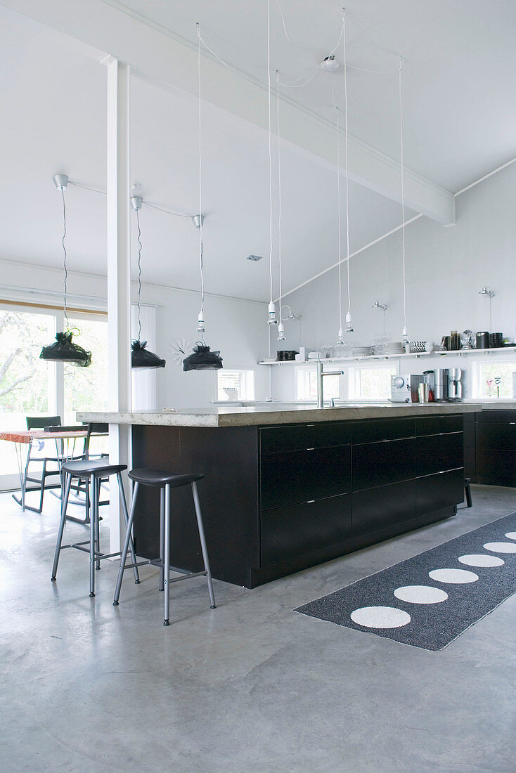 Black cabinets and concrete floor in large kitchen below exposed roof structure