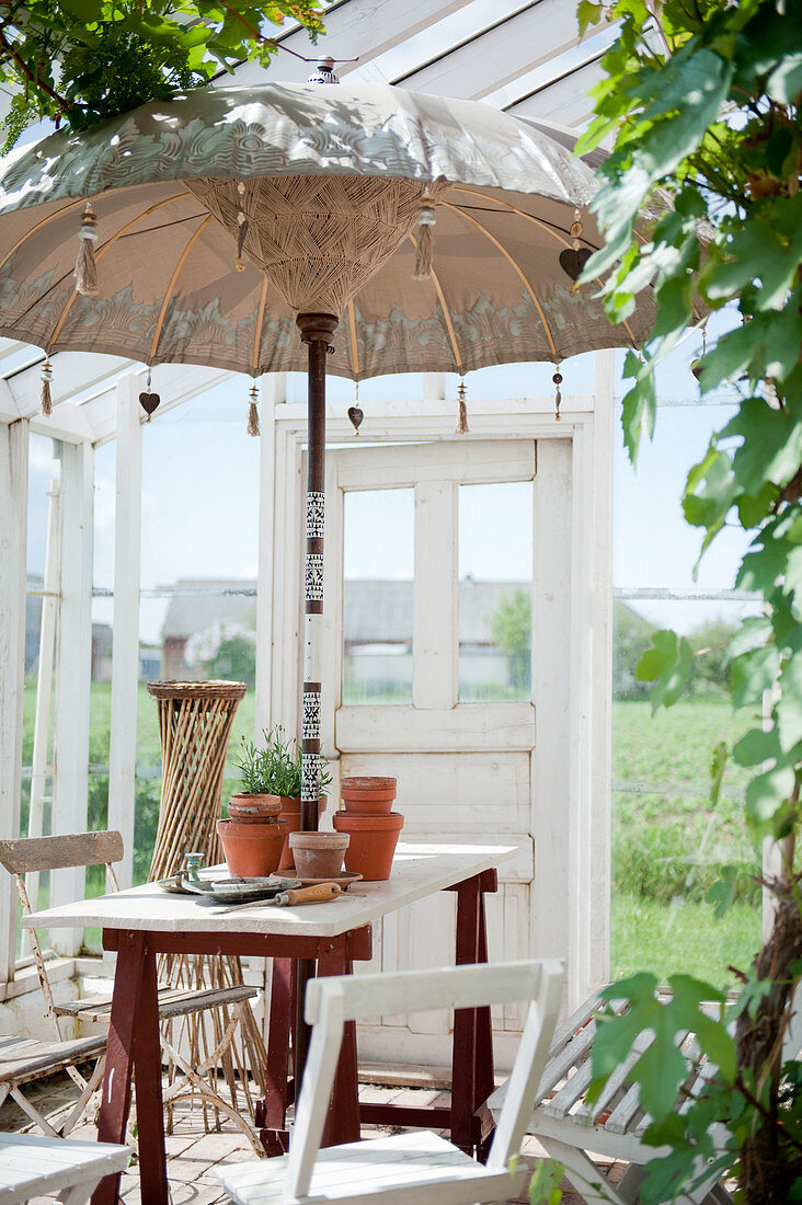 Balischirm über dem Tisch auf Möbelböcken im Glashaus im Garten