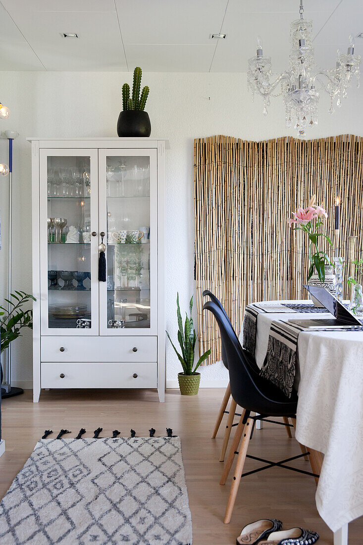 Table, black shell chairs, bamboo screen and glass-fronted cabinet in dining room