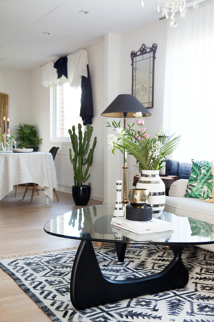 Glass coffee table on black-and-white rug with dining area in background