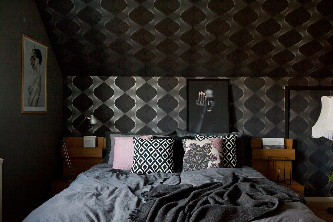 Double bed with dark bed linen in bedroom with black wallpaper