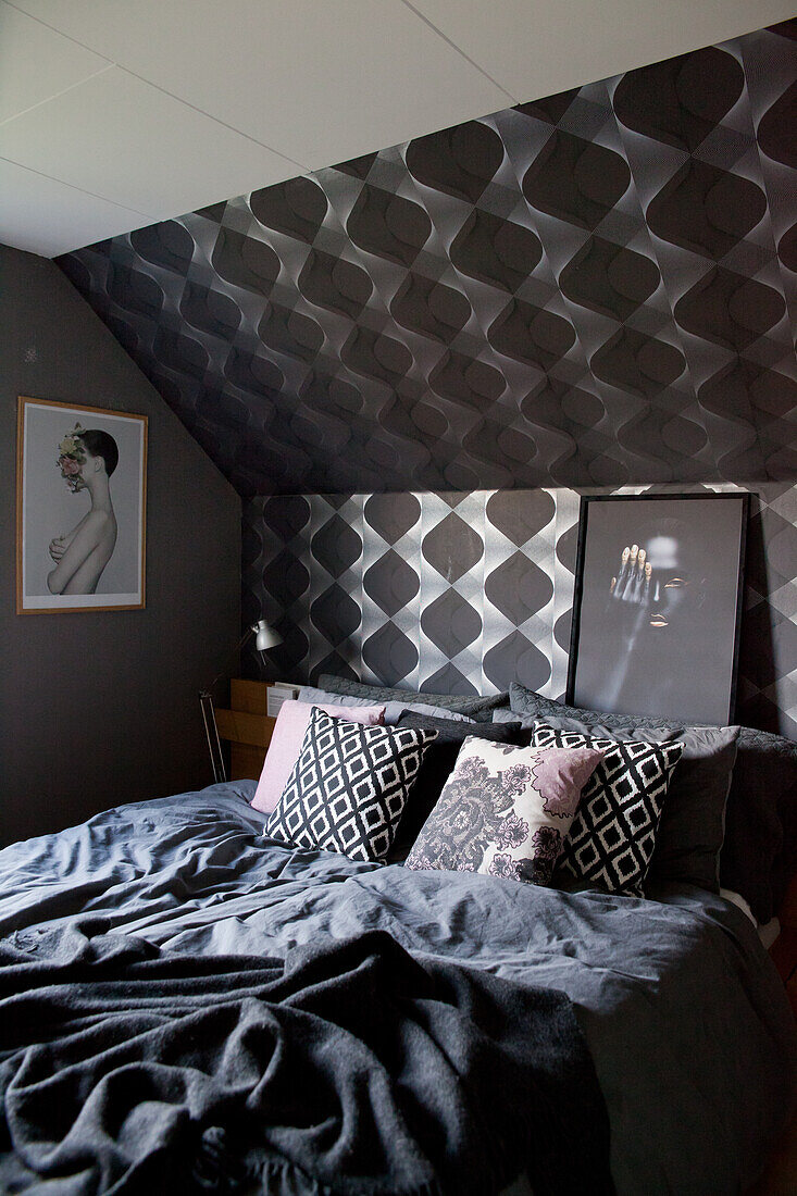 Double bed with dark bed linen in bedroom with black wallpaper