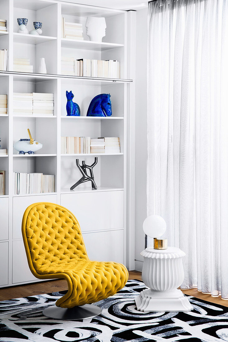 Gelber Designerstuhl und Beistelltisch vor weißer Regal im Wohnzimmer