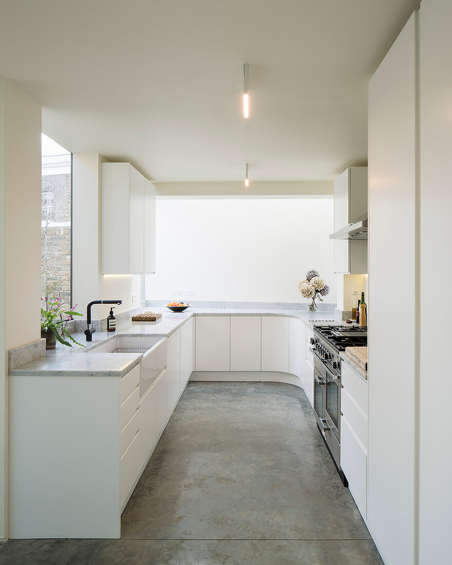 White, minimalist kitchen with rounded corner and concrete floor