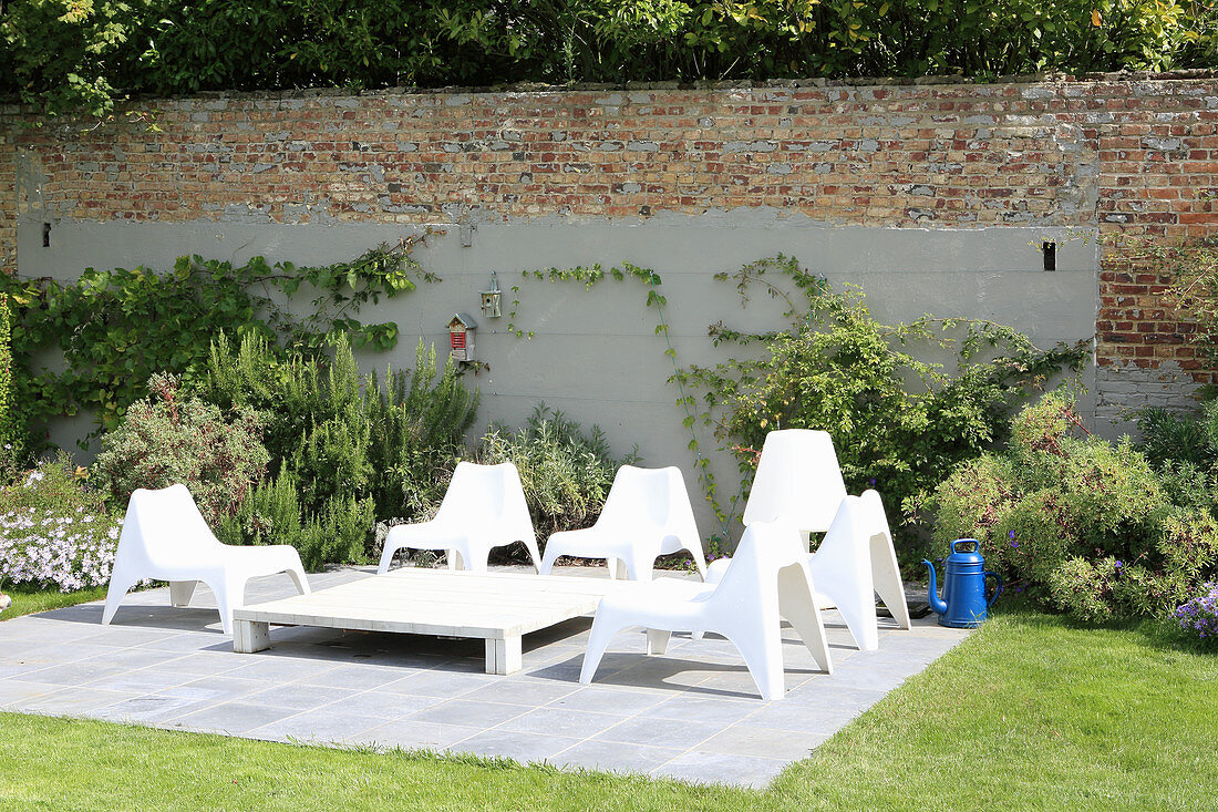 weiße Plastikstühle auf der Terrasse an der Gartenmauer