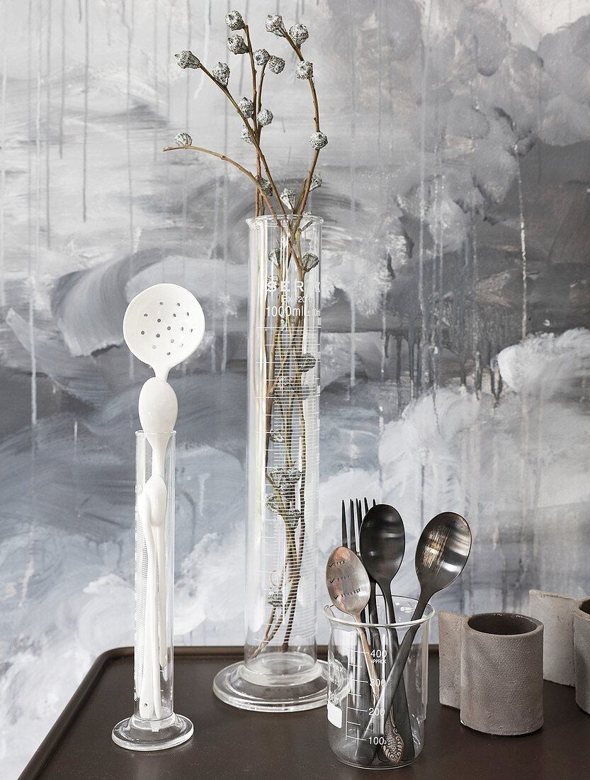 Cutlery, kitchen utensils and twigs in tall glass measuring beaker