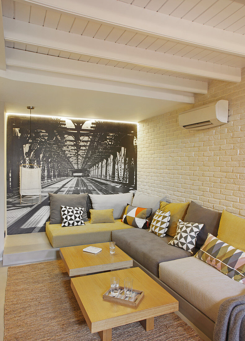 Modern grey and mustard-yellow sofa in front of photo mural and brick wall