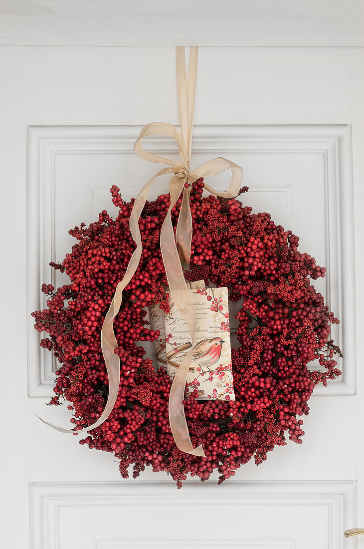 Wreath of red berries with postcard on white door