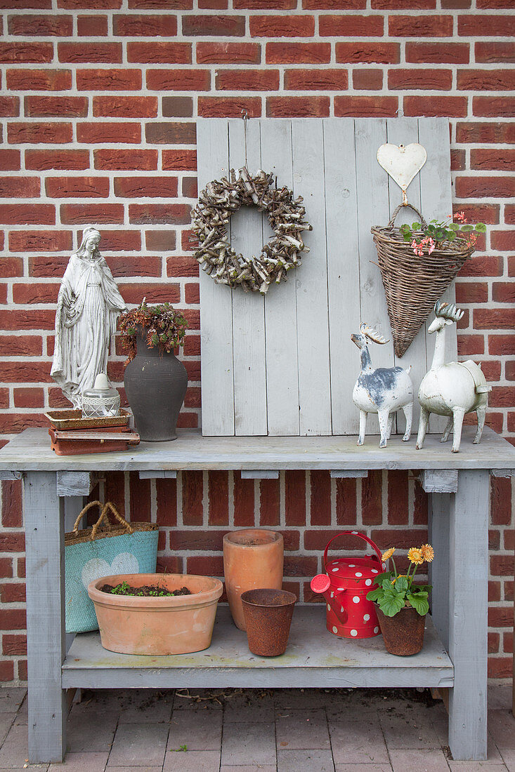 Various ornaments and plant pots on wooden potting table against brick wall