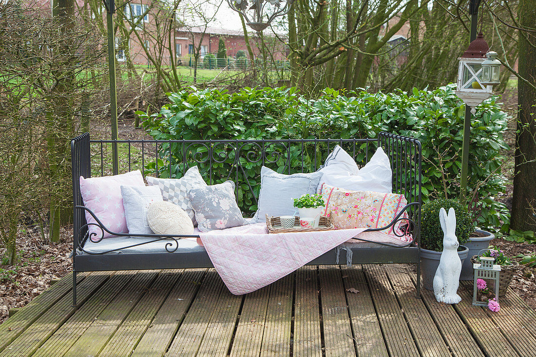 Gartenbank mit Kissen, Decke und Korbtablett, daneben Hasenfigur auf Terrassenplatz