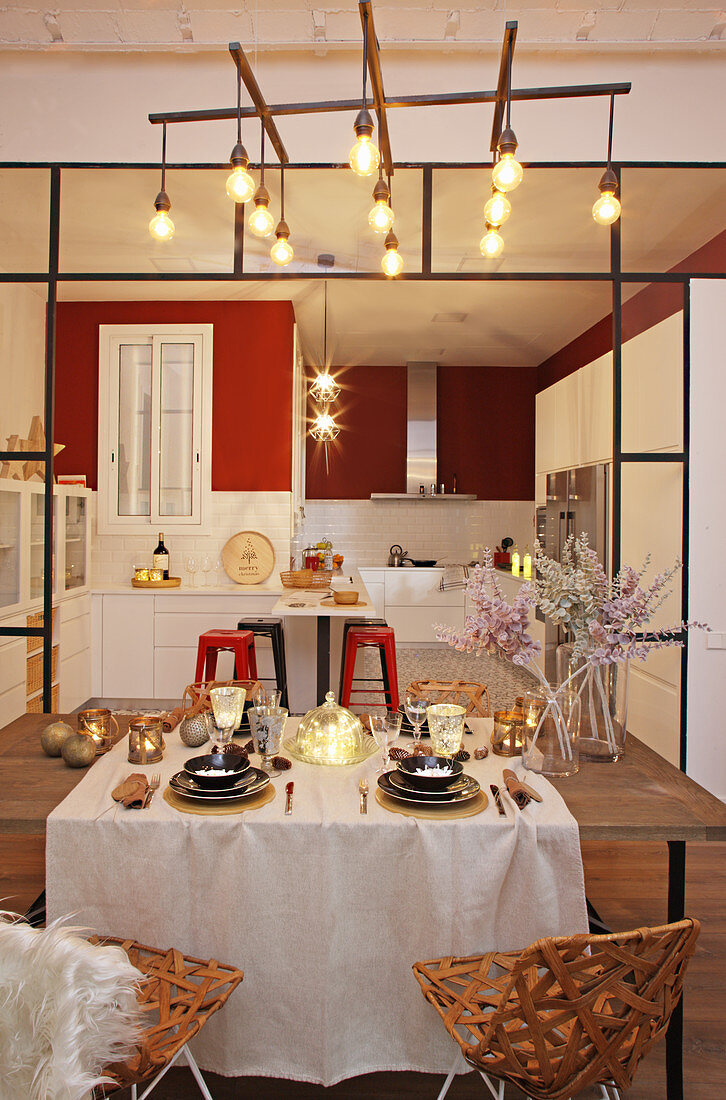 Festively set table in front of open-plan kitchen with red wall