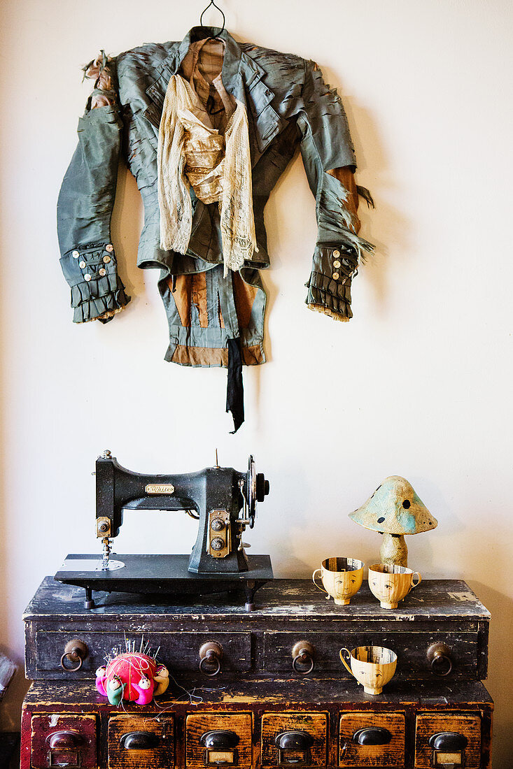 Designer jacket on wall above vintage sewing machine and papier-mâché cups on chest of drawers