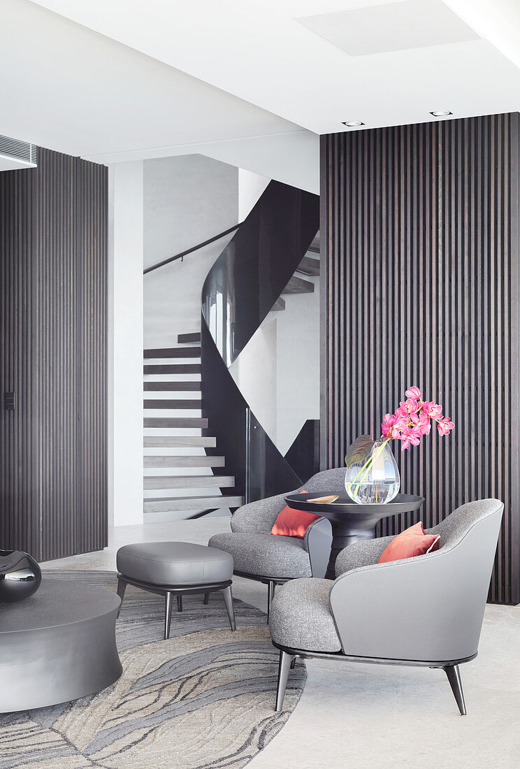 Dunkelgraue Designersessel und Beistelltisch mit Blumenvase im Wohnzimmer vor Treppenaufgang