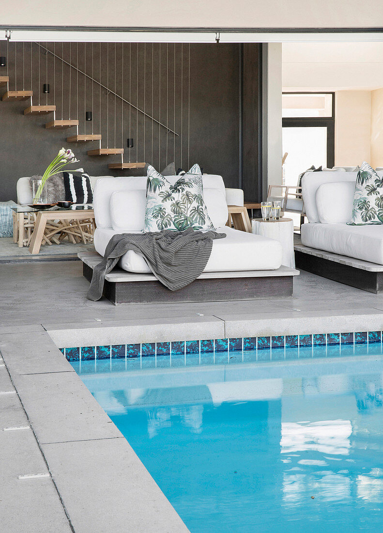 Leaf-patterned scatter cushions on upholstered loungers next to pool