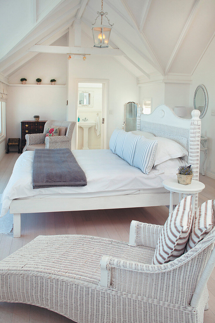 Korbsessel und Bett im weißen Schlafzimmer unter dem Dach