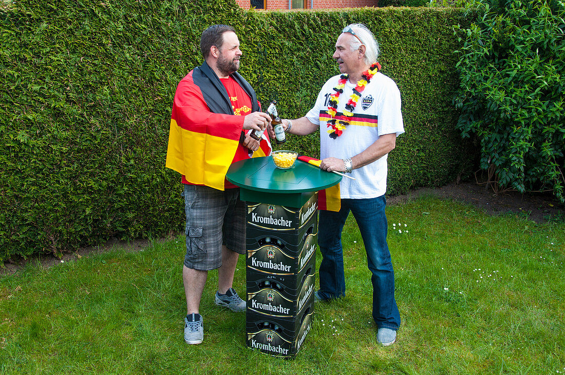Two German fans stood at tall table made from beer crates in garden